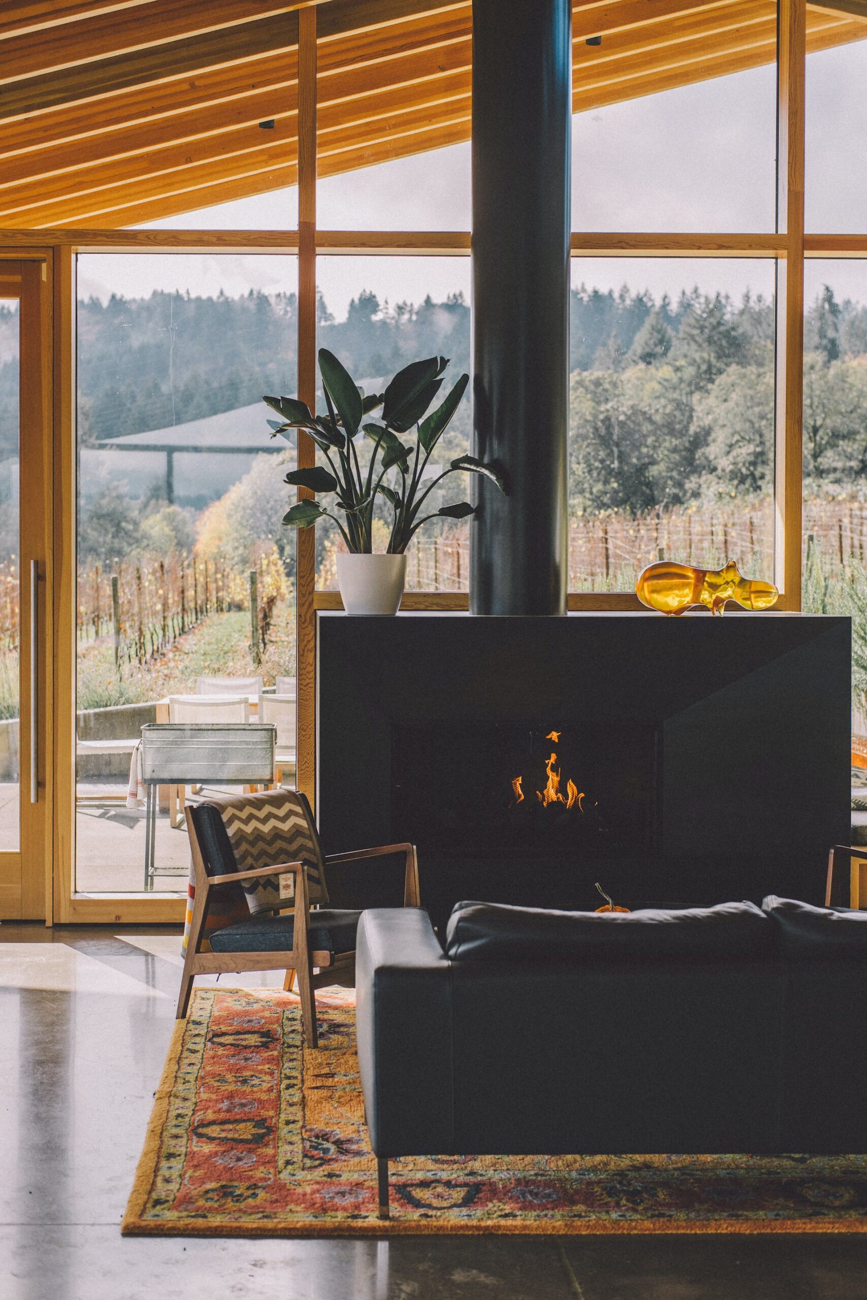 Inviting living room featuring a fireplace, comfortable lounge furniture, and a stylish rug. Expansive windows provide a scenic view of a lush farm surrounded by vibrant greenery